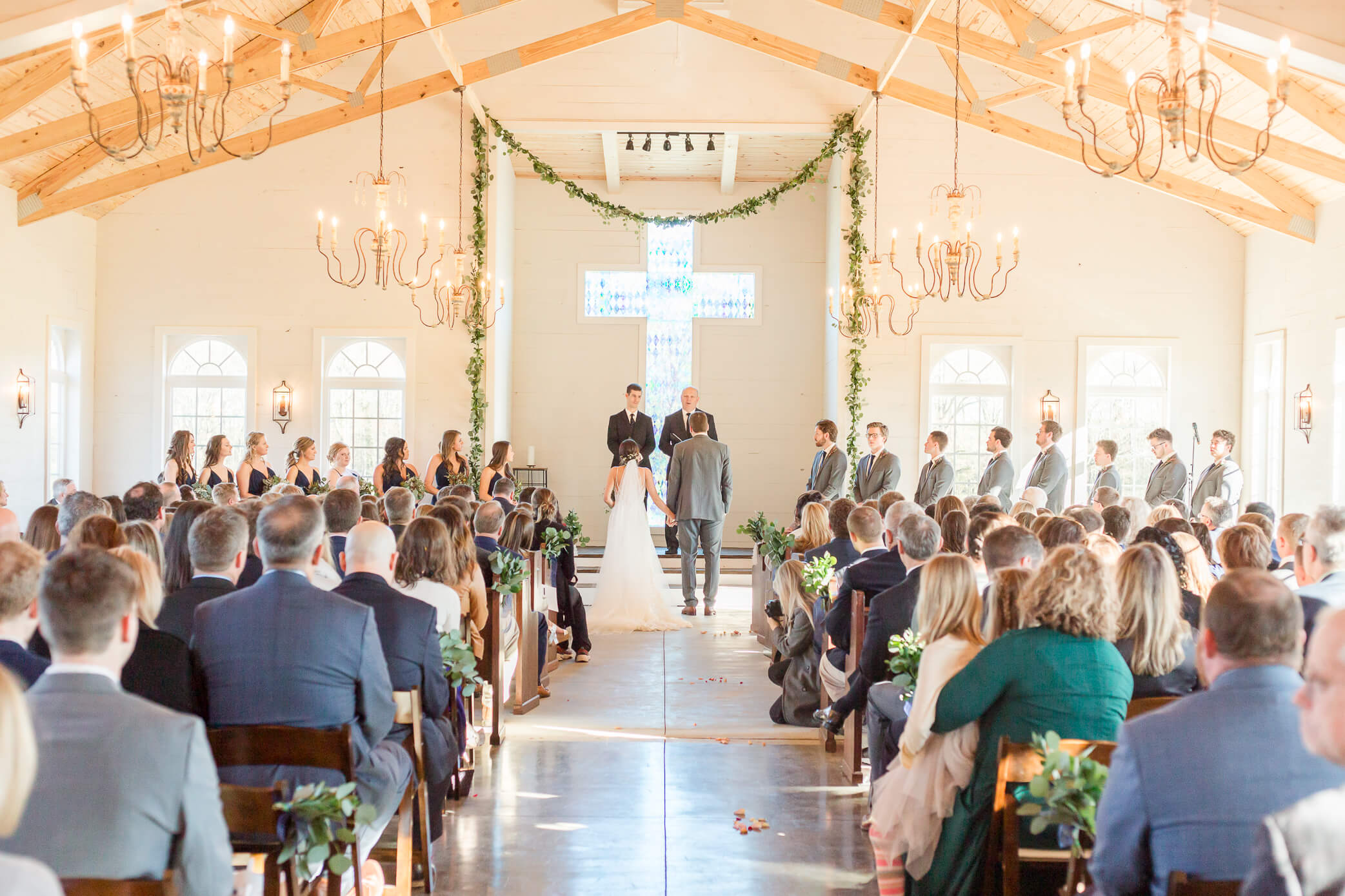 Bride and groom holding hands at the altar during their barn wedding venue in Oxfordshire. Guests are seated and watching.