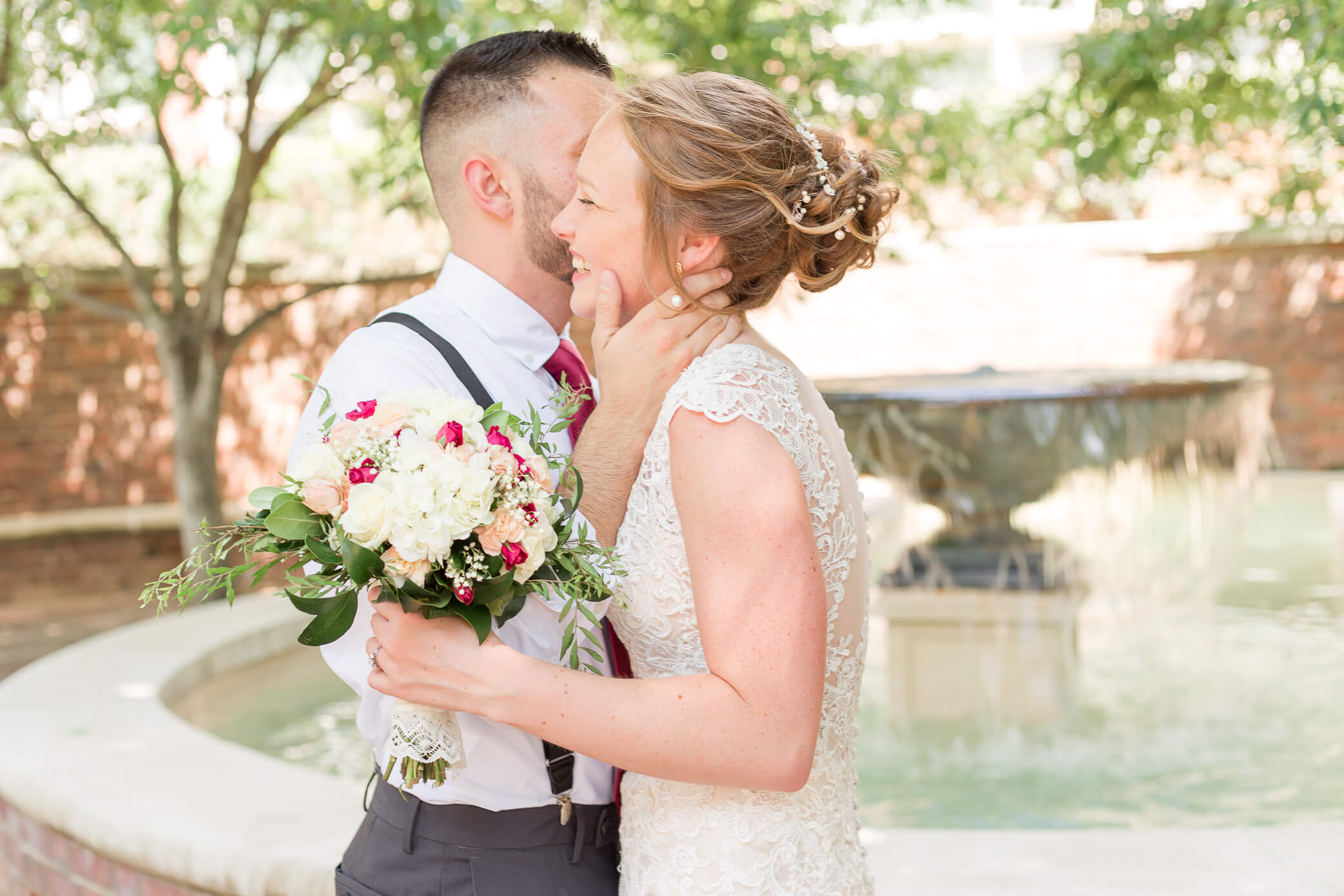 A groom kisses his bride on the cheeck as they lean in close during their first look. The bride's updo was done by a hair salon in Oxford.