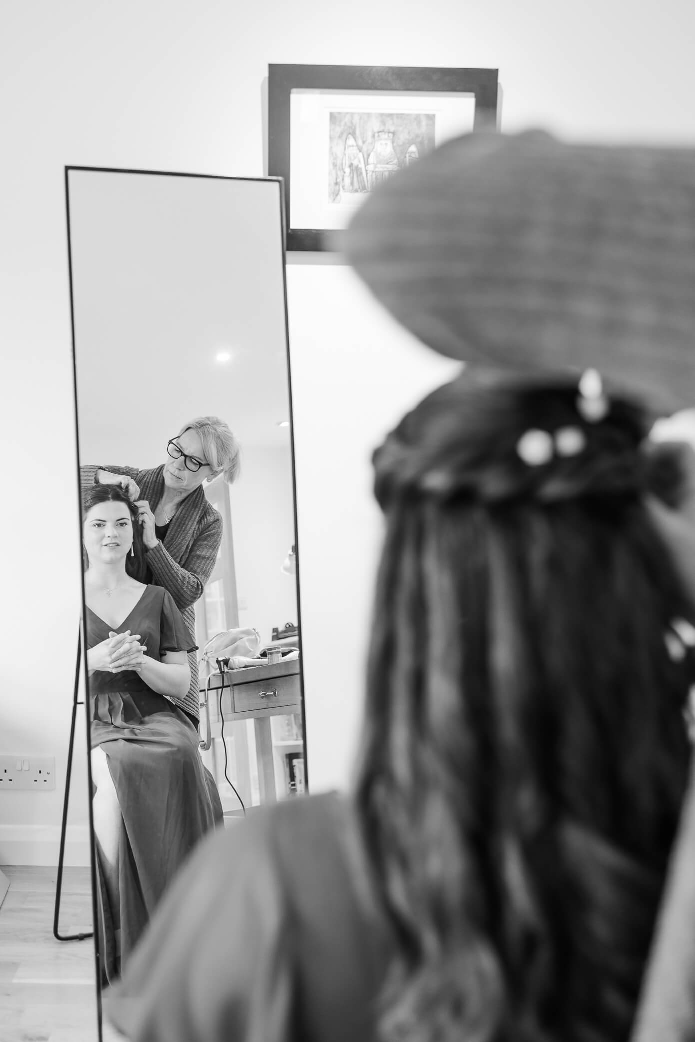 A bridesmaid sits in front of a long mirror as her hair is being styled at a hair salon in Oxford