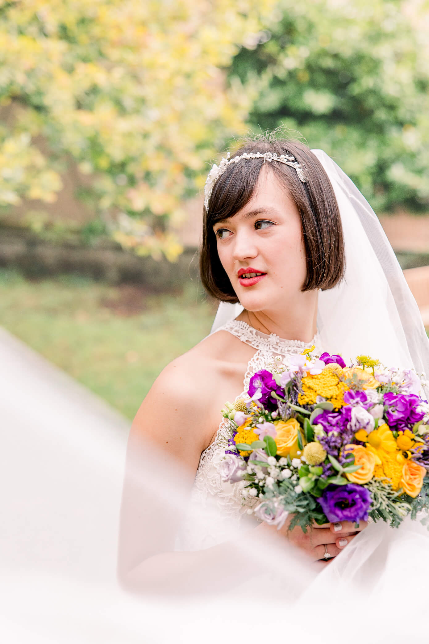 A bride holding a bouquet of flowers from an Oxford florist and looking over her shoulder as her veil blows in the wind across her body.