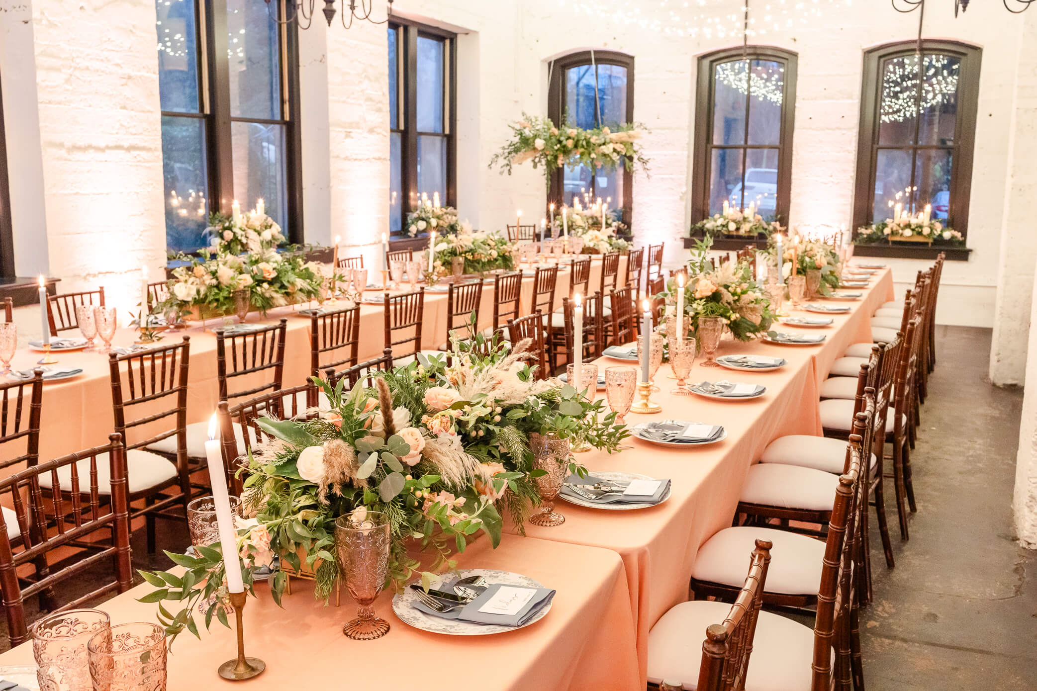 Long rectangular dining tables covered in peach table cloths with big beautiful floral displays, candles, and china.