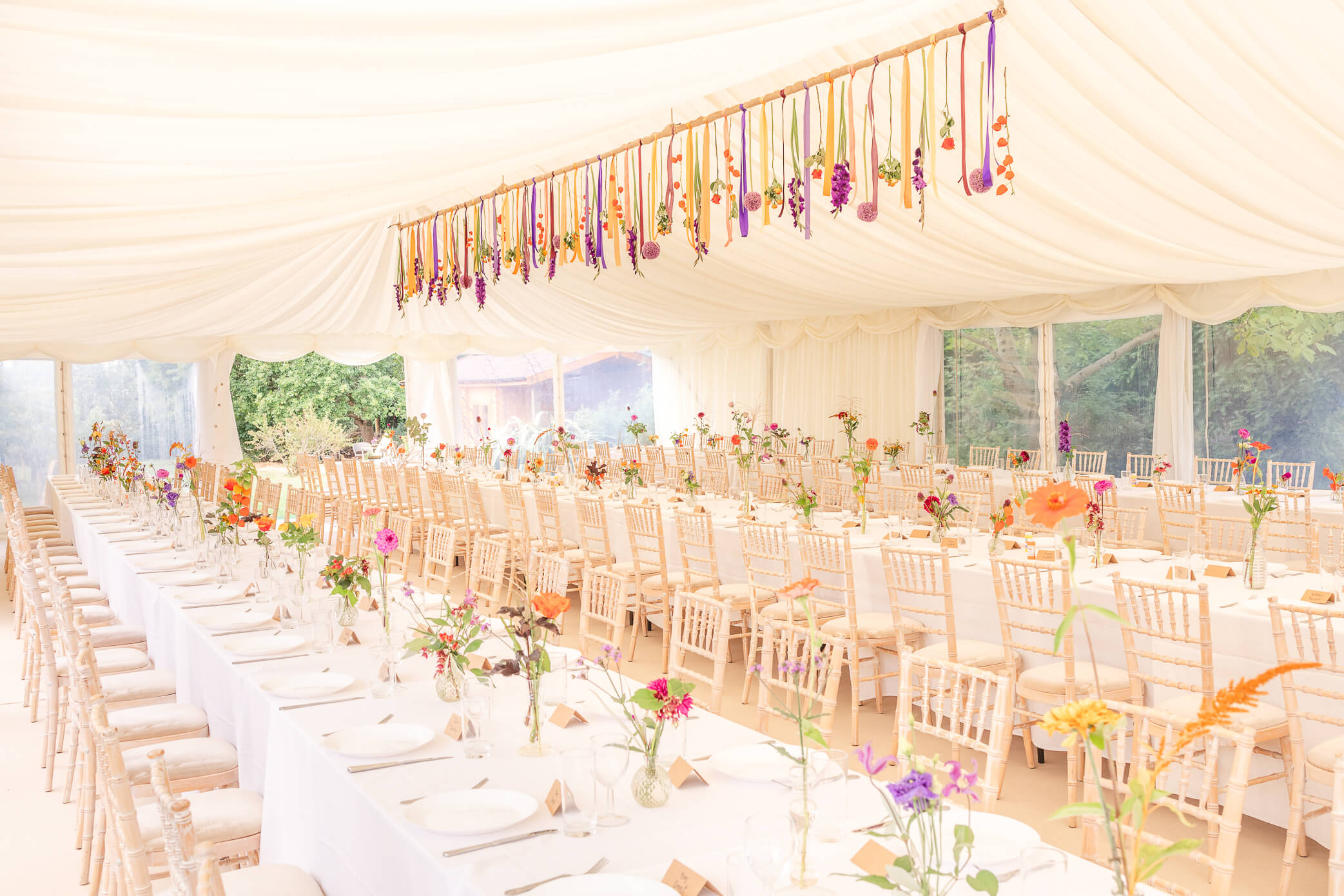 White wedding marquee set up with beautiful floral centerpieces lining the long rectangular tables and a grand floral installation hanging from the ceiling that was installed by an Oxford florist.