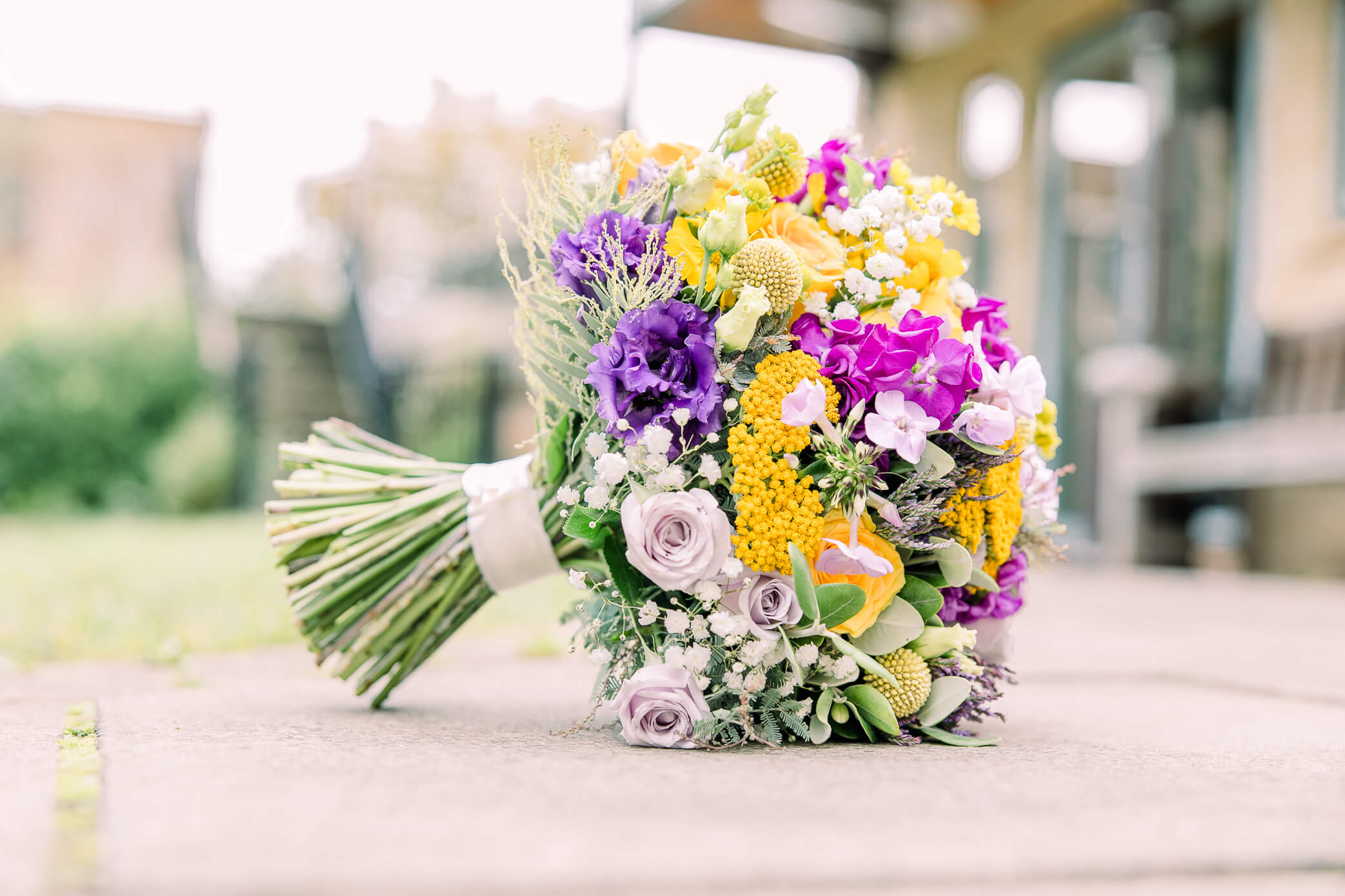 A bridal bouquet of yellow and purple flowers lying on its side on some pavement