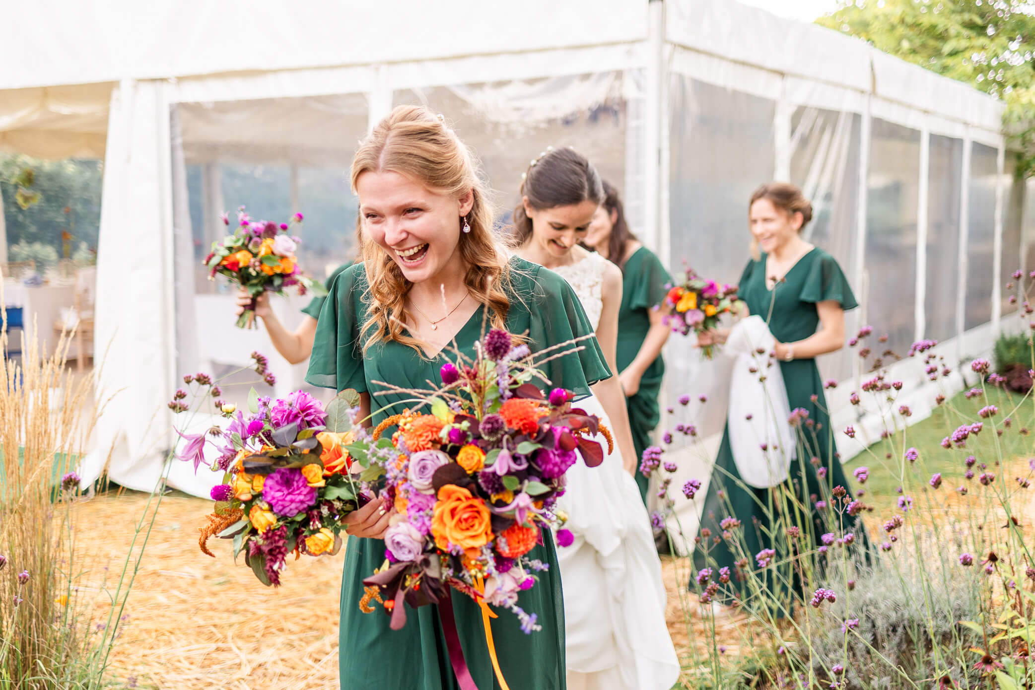 A bridesmaid leading the way and carrying her bouquet as well as the bride's as they walk towards the ceremony.