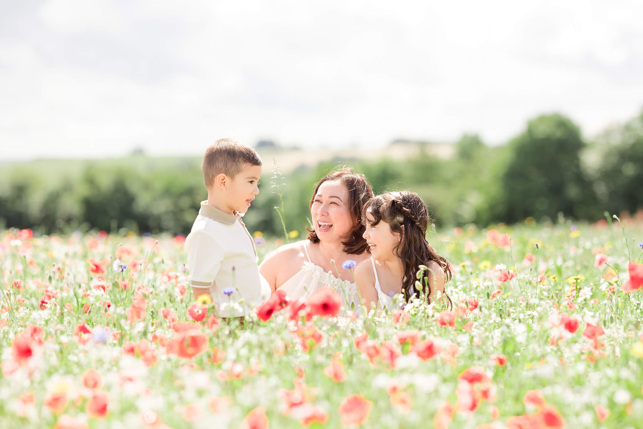 A mother kneels down in a beautiful flower meadow with her daughter and son as they play. Visiting the meadow is one of the fun things to do in Oxford with kids.