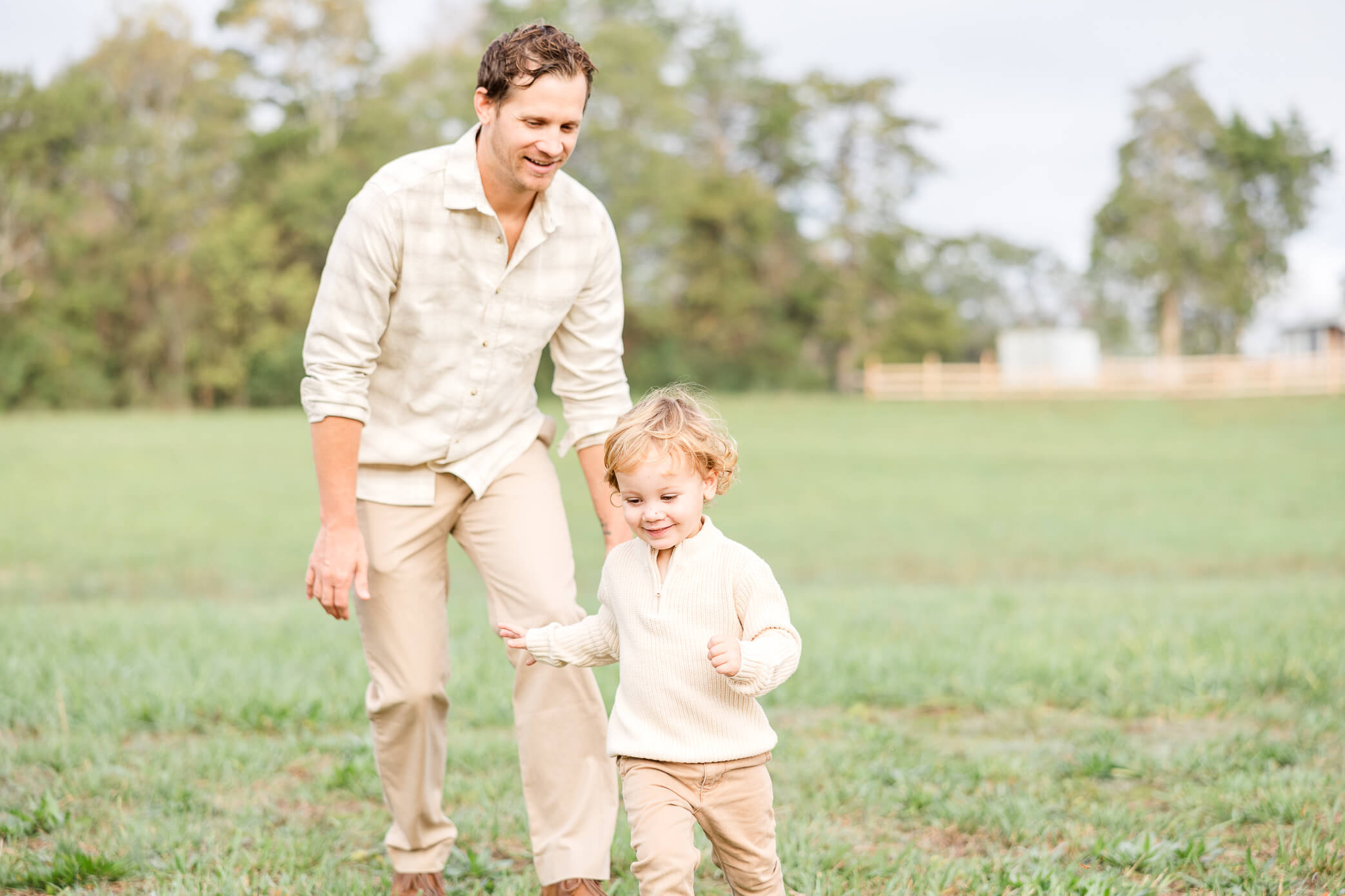 A father chases his young son as he runs away and laughs in a park.