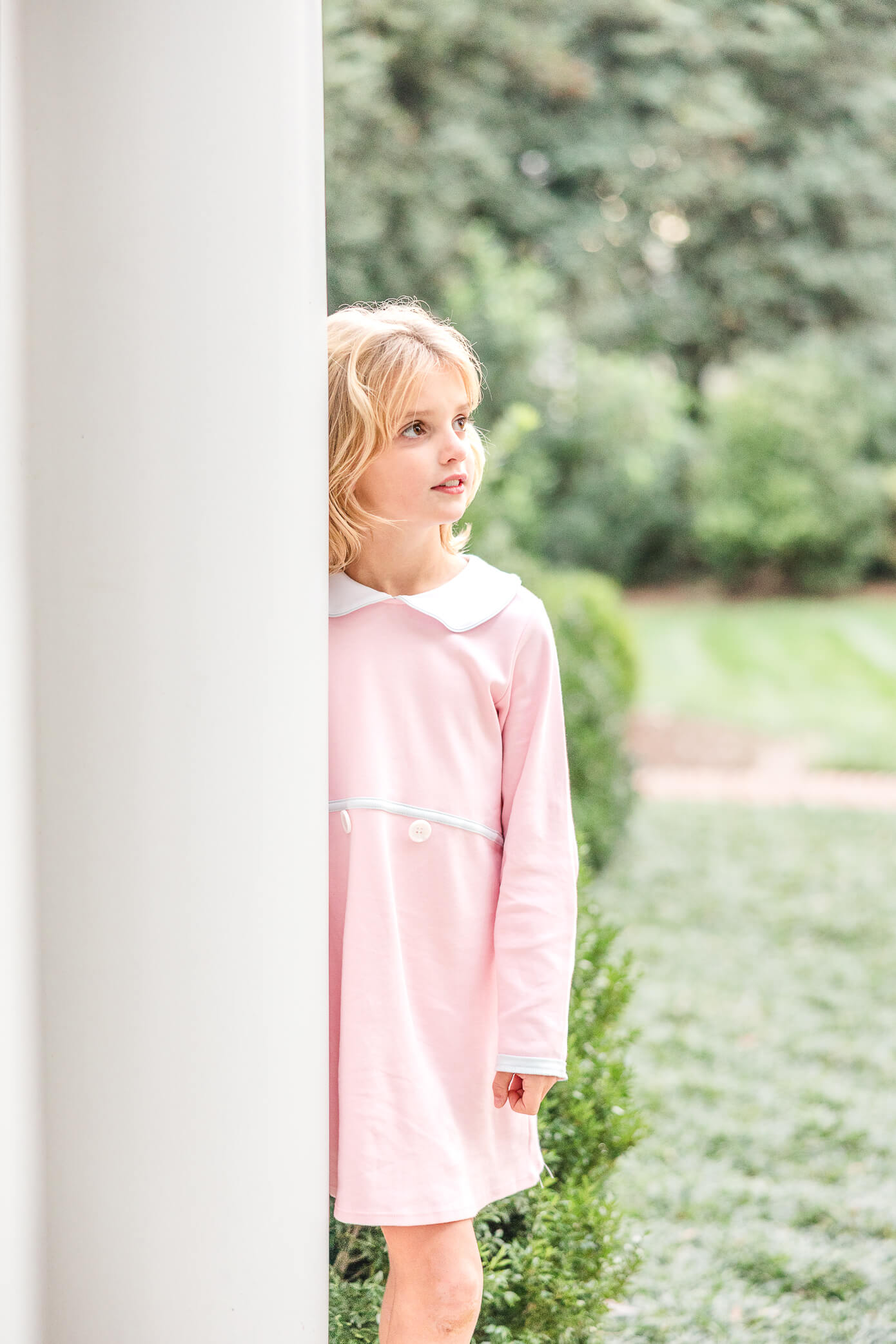 A beautiful young blonde girl stands and leans against a big white column as she looks out into a park. She is looking for fun things to do in Oxford with kids.