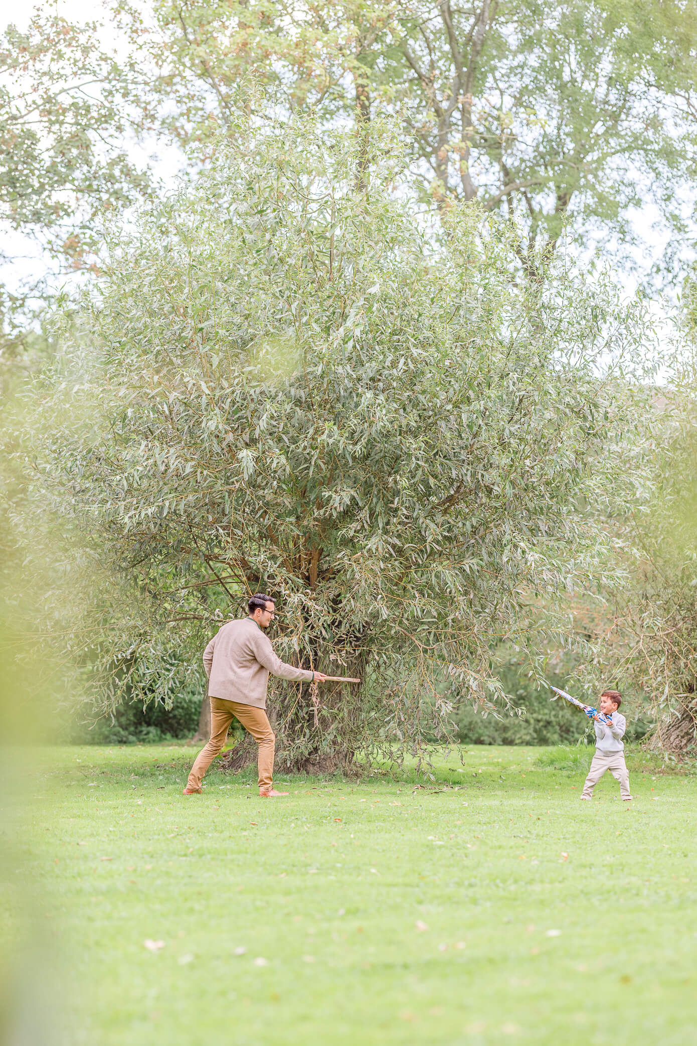 A father and son pretend to sword fight in a park as one of the fun things to do in Oxford with kids.