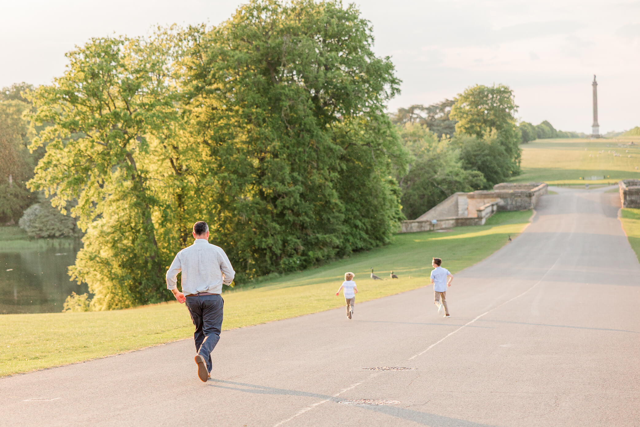 A father chases his two sons down a road in a park. They run towards a bridge and some geese on the edge of the lake. This is one of the fun things to do in Oxford with kids.