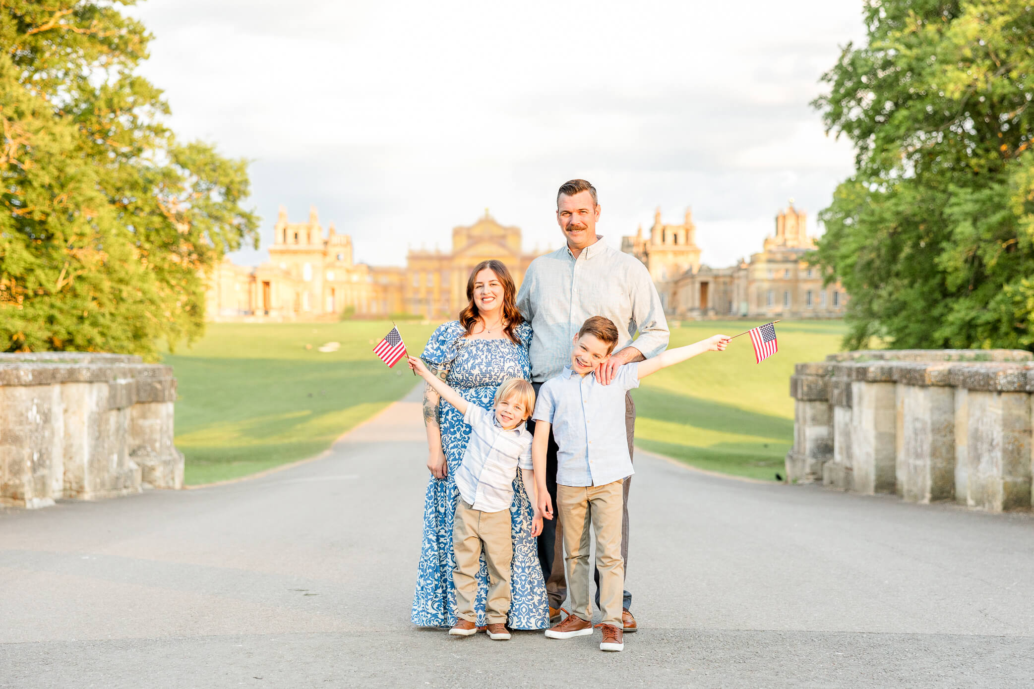 A family with two young sons stand in front of Blenheim Palace and wave little flags as one of the fun things to do in Oxford with kids.