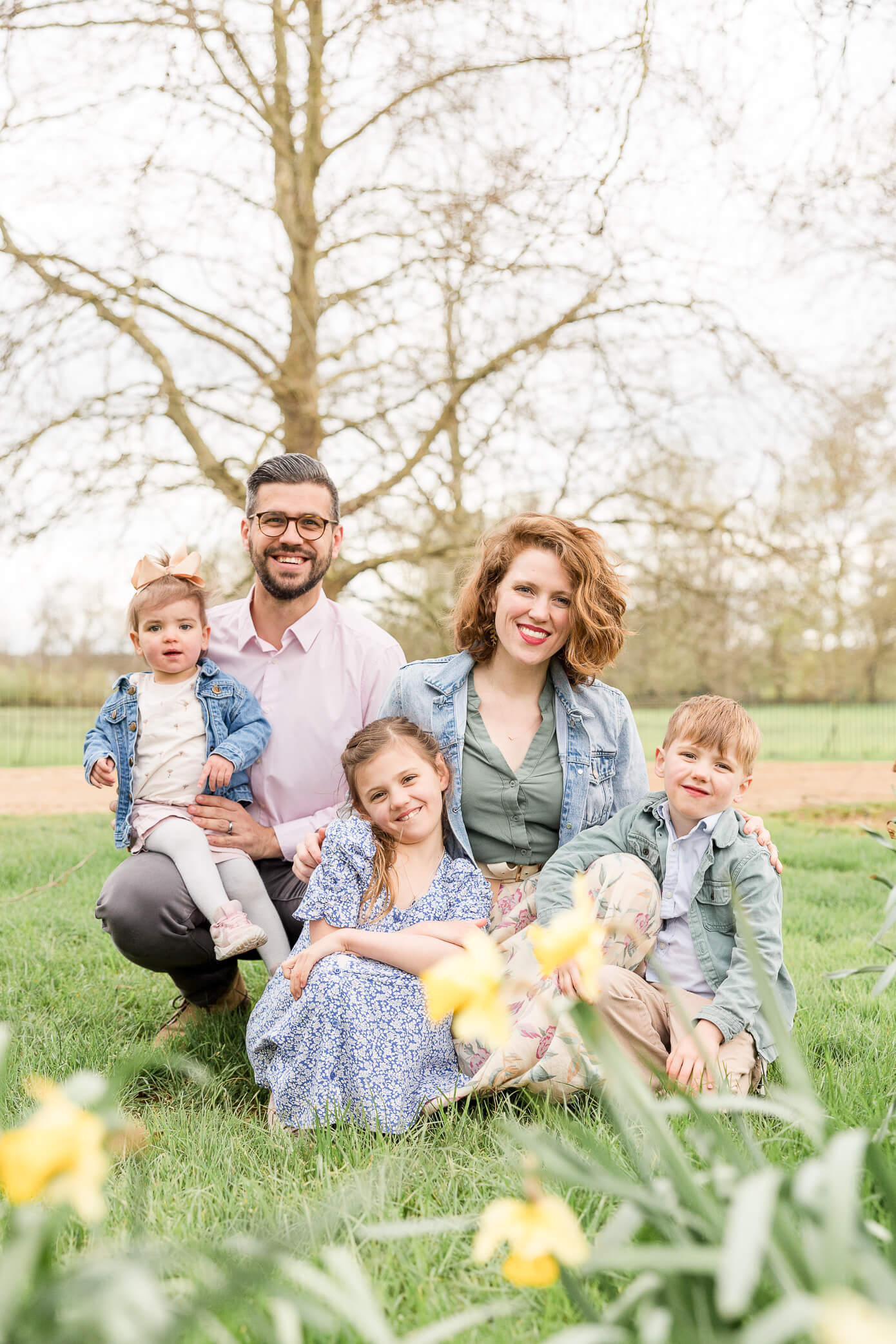 A young family of five squats down together in a park in front of some beautiful blooming daffodils while looking for things to do in Oxford with kids.