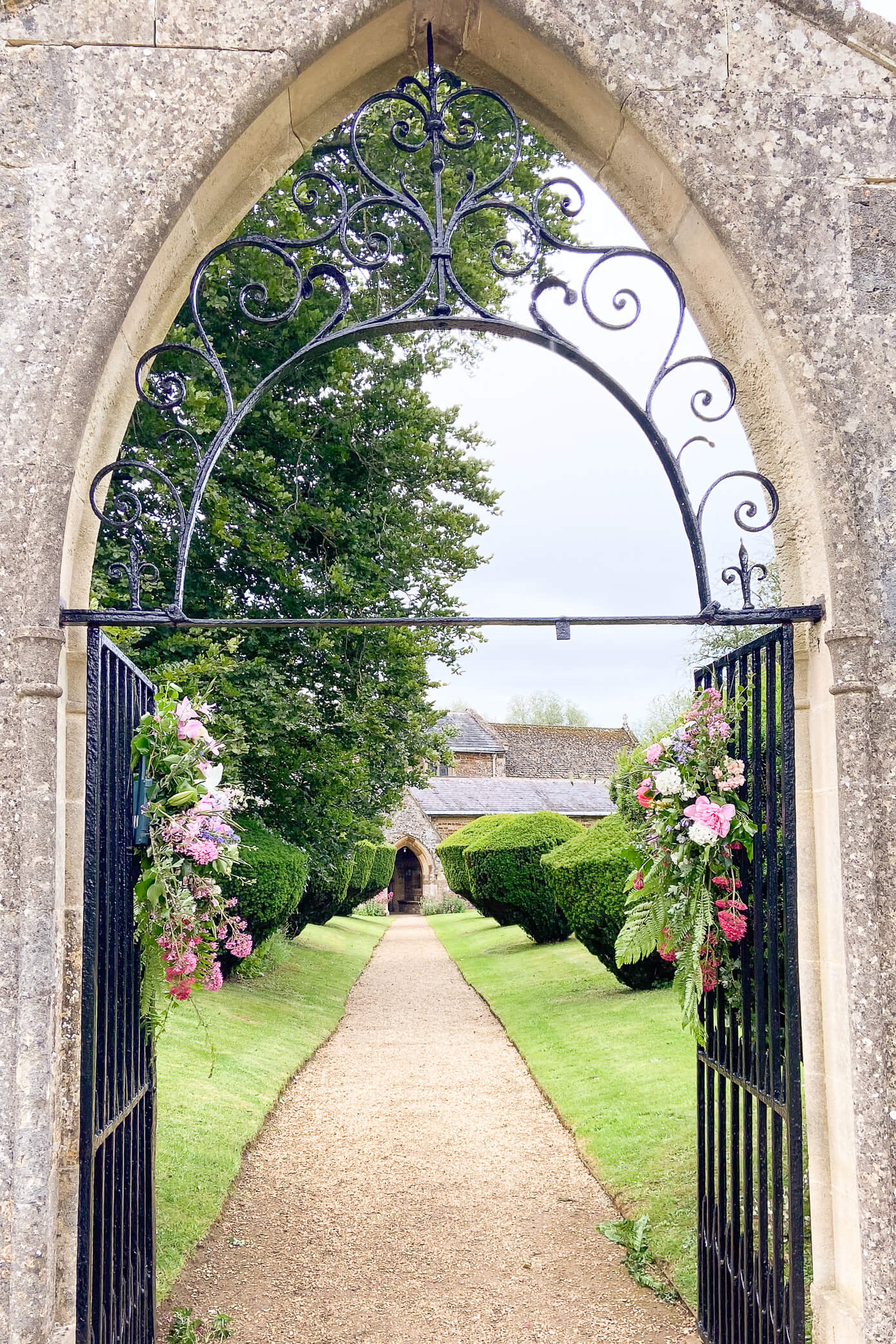 A stone archway with floral arrangements leading through the entrance of the church yard at a Rousham House wedding.