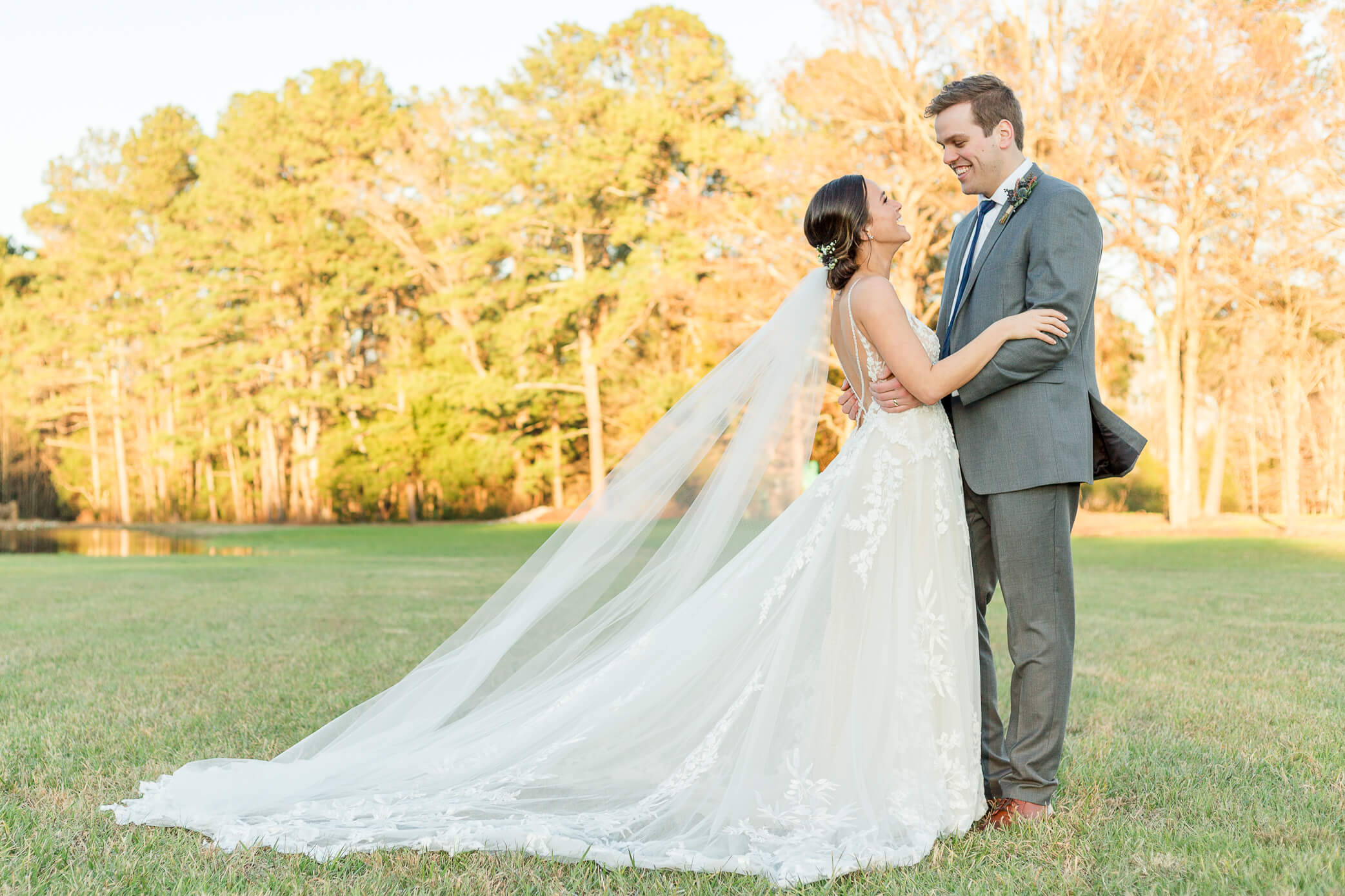 A bride and groom stand in a field facing and holding each other as they laugh and enjoy their Woodstock wedding