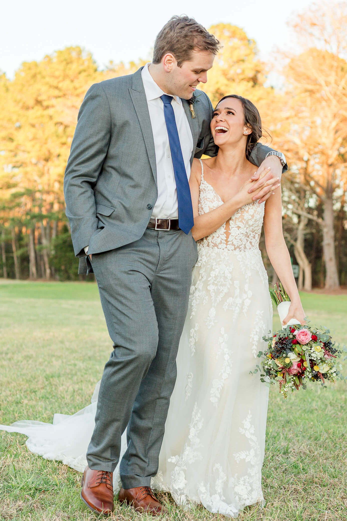 Groom with his arm around his bride's shoulders as they walk and laugh on their wedding day