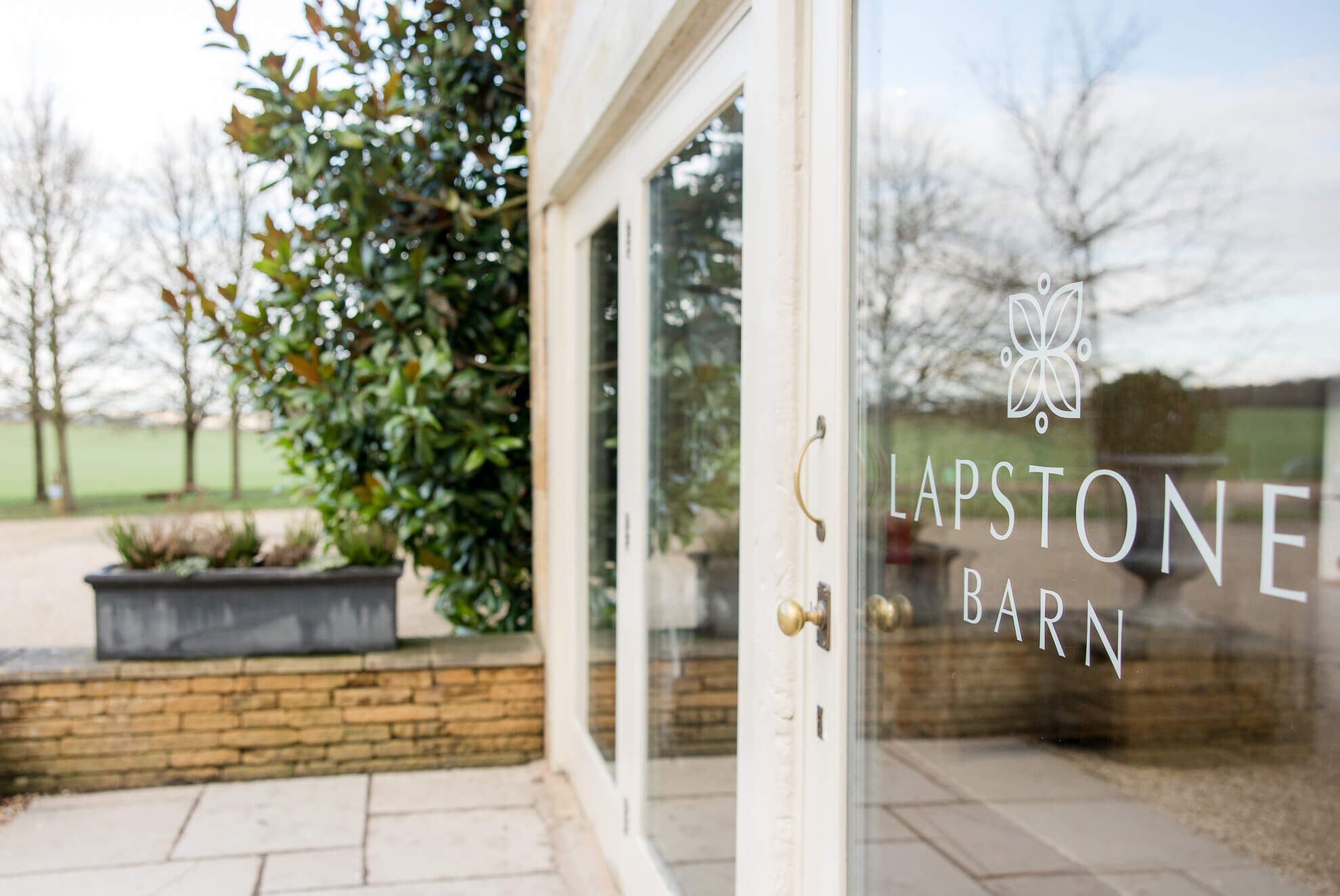 The entry doors to Lapstone Barn wedding venue with the name of the barn on the window. The windows are reflecting the beautiful countryside around the venue.