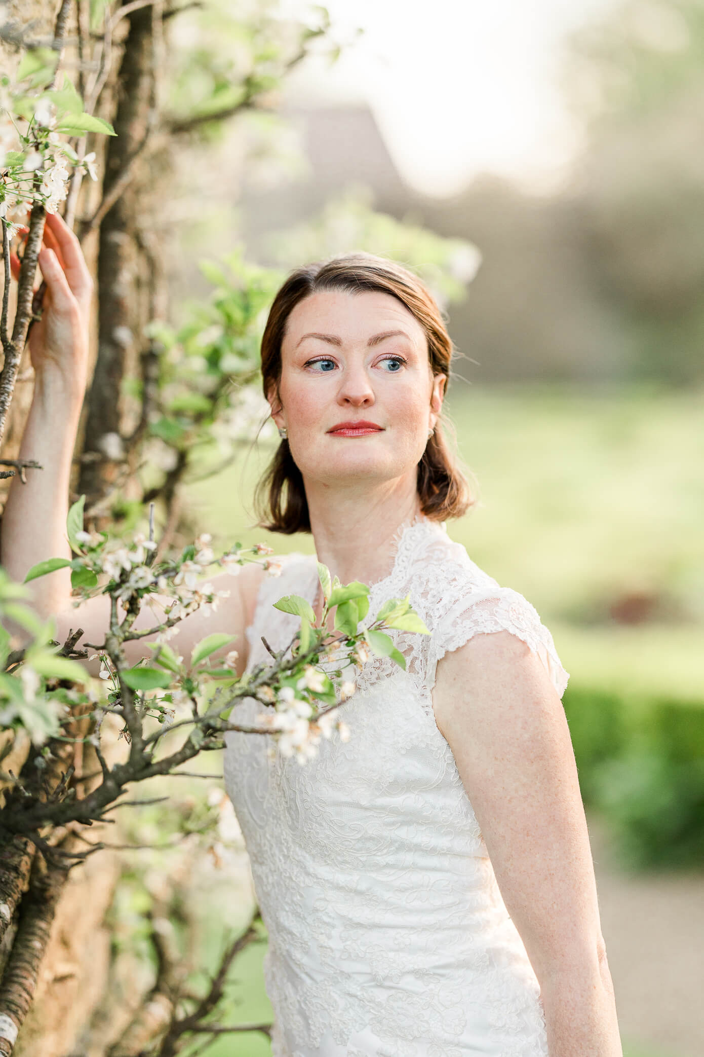 An up close shot of a beautiful bride as she rests her hand on a building that has branches and buds growing off of it at a Rousham House wedding.