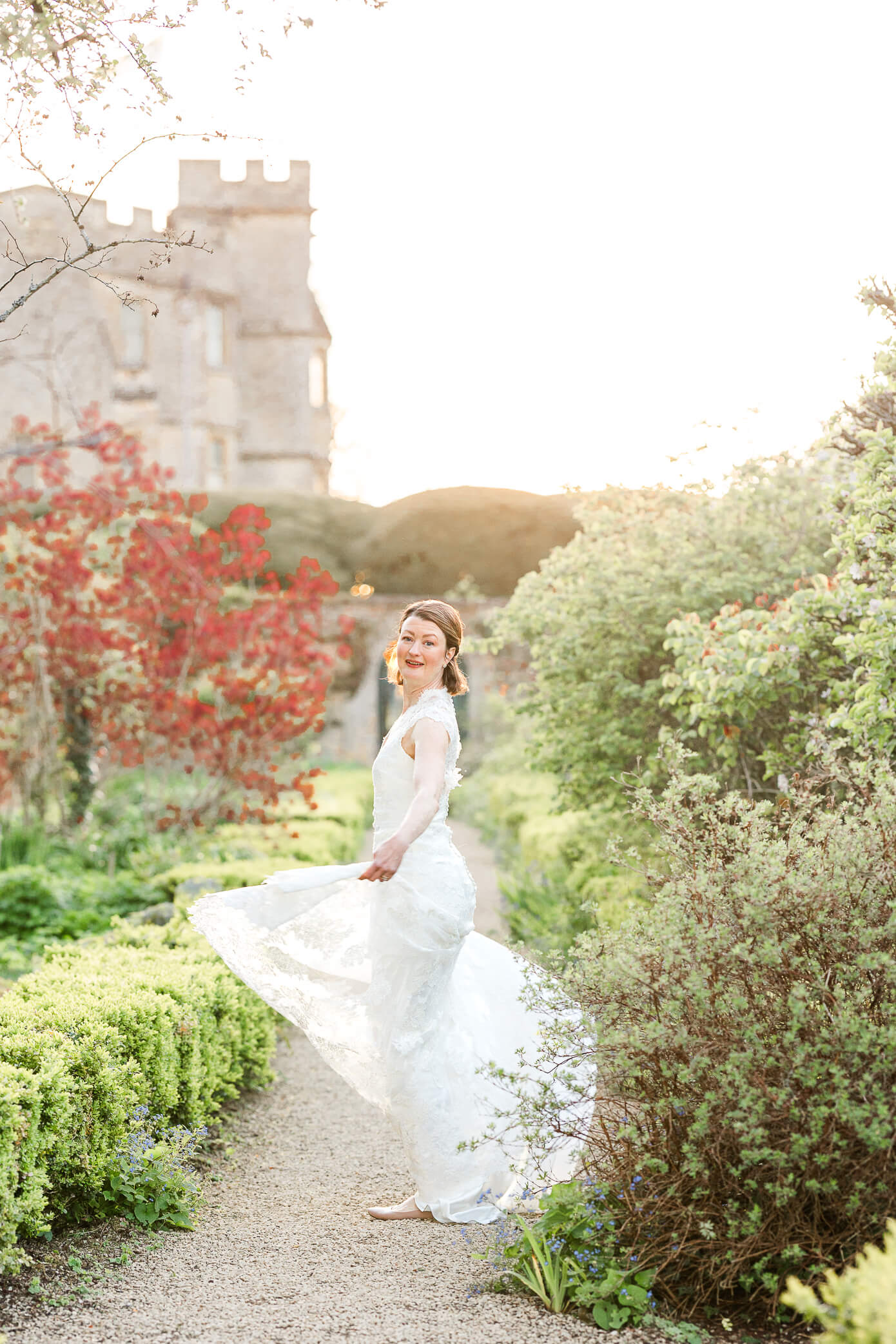 A bride twirls in her wedding gown on a garden path while standing in front of a gorgeous cotswolds manor house.