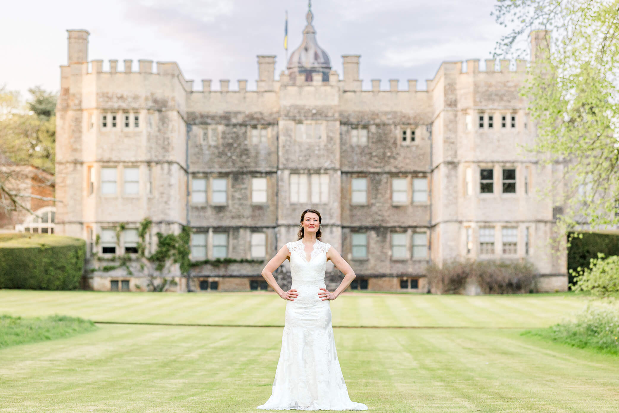 A bride poses in front of Rousham House wedding with her gown on. She stands on the green wit her hands on her hips in a very editorial pose.