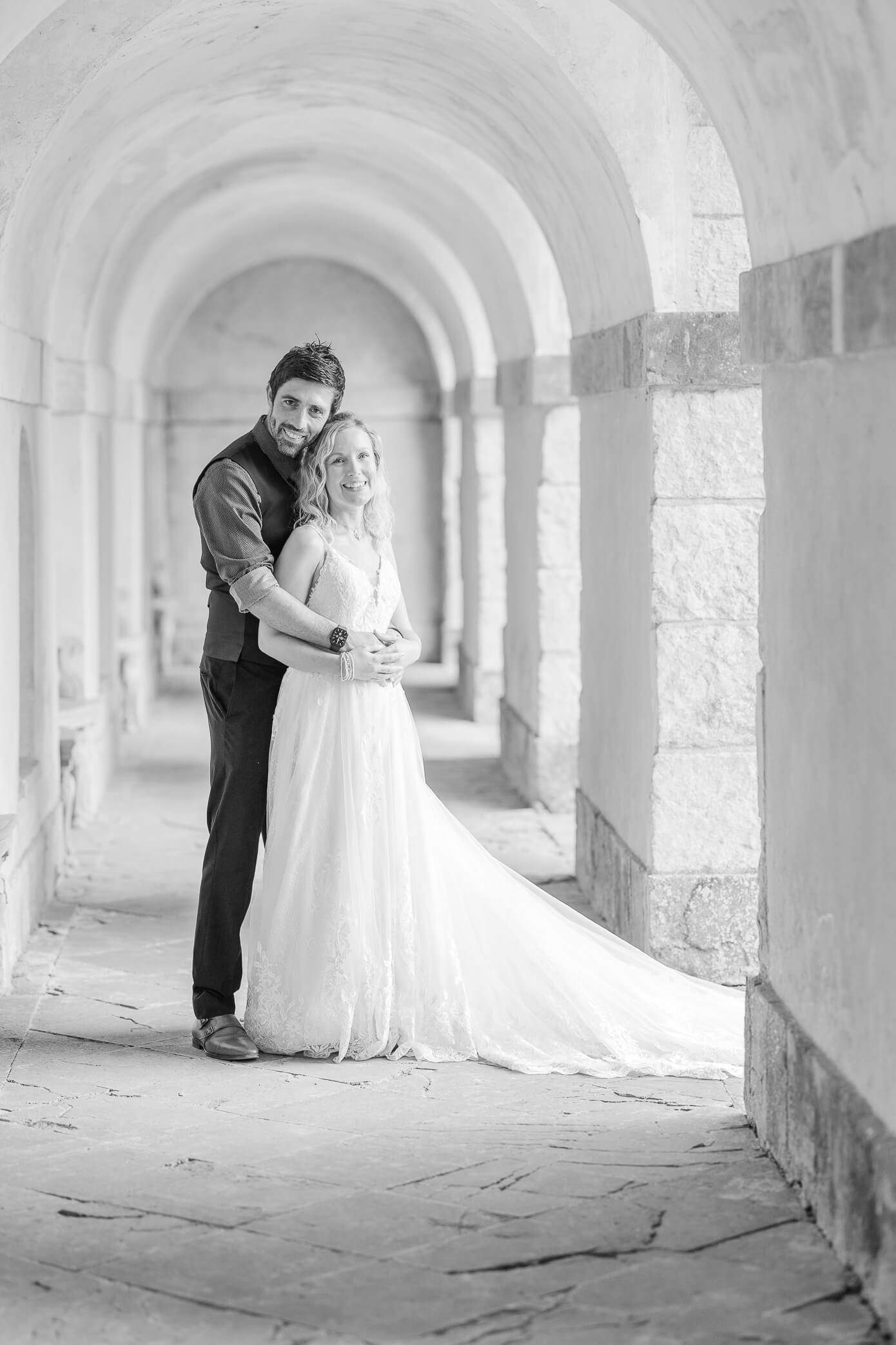 A bride and groom cuddle close while standing beneath a arched structure at a Rousham House wedding.