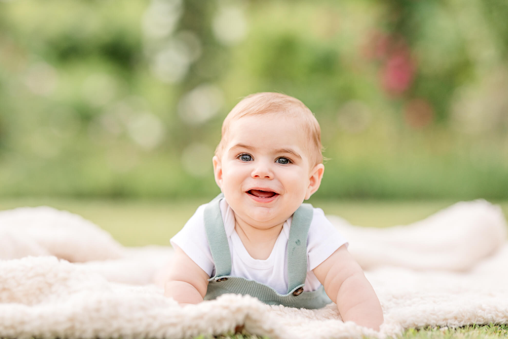 A sweet baby boy lays on his tummy on a blanket, lifts his head up, and smiles really big. He just had his vaccinations at the Woodstock pediatricians office.