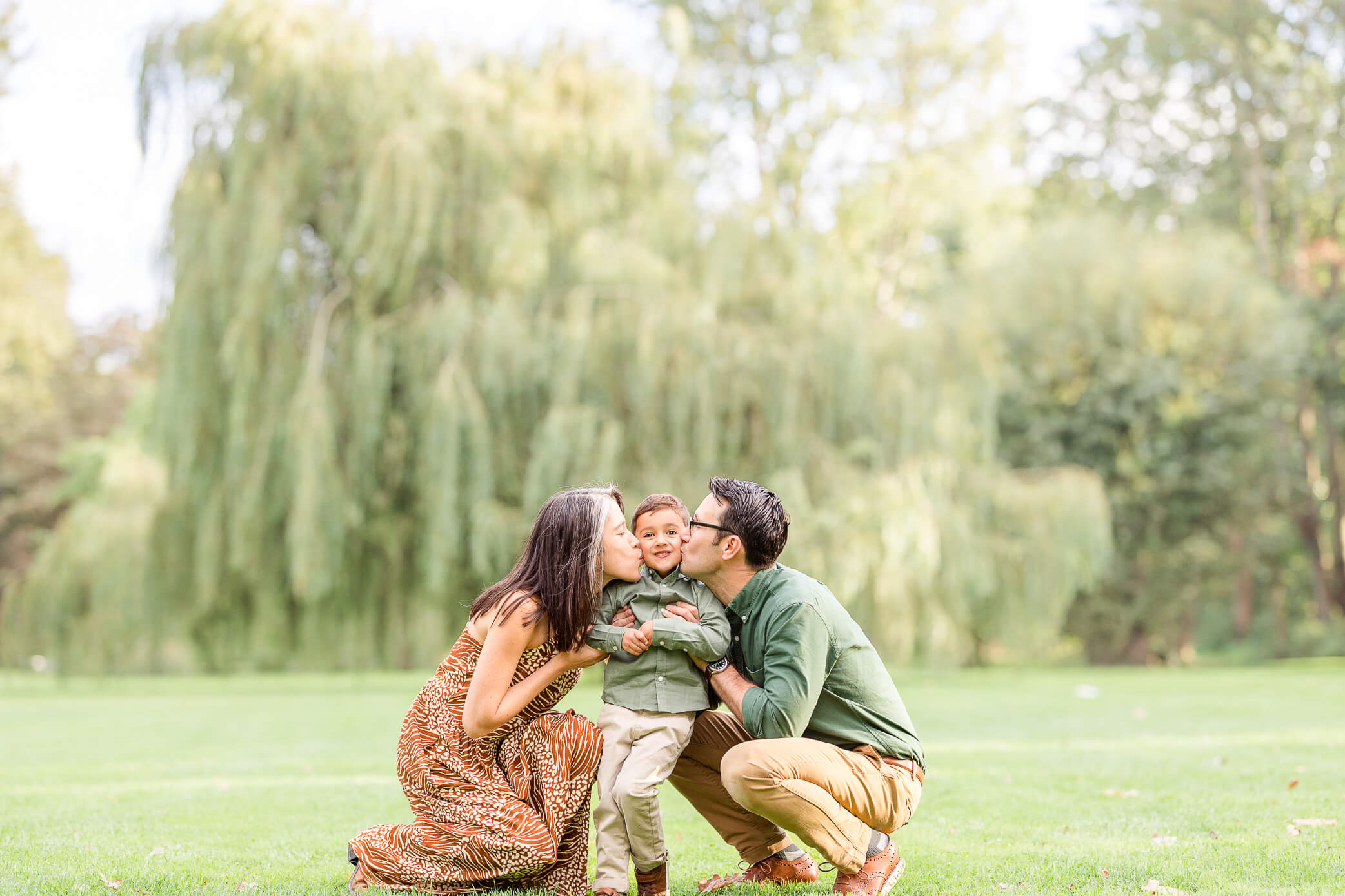 A mother and father kiss their young son on the cheek at the same time after he visited the Woodstock pediatricians.