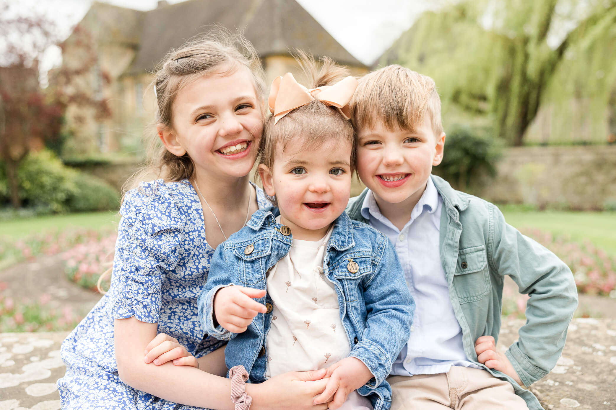 Three siblings sit together and snuggle in real close for a group hug while smiling.