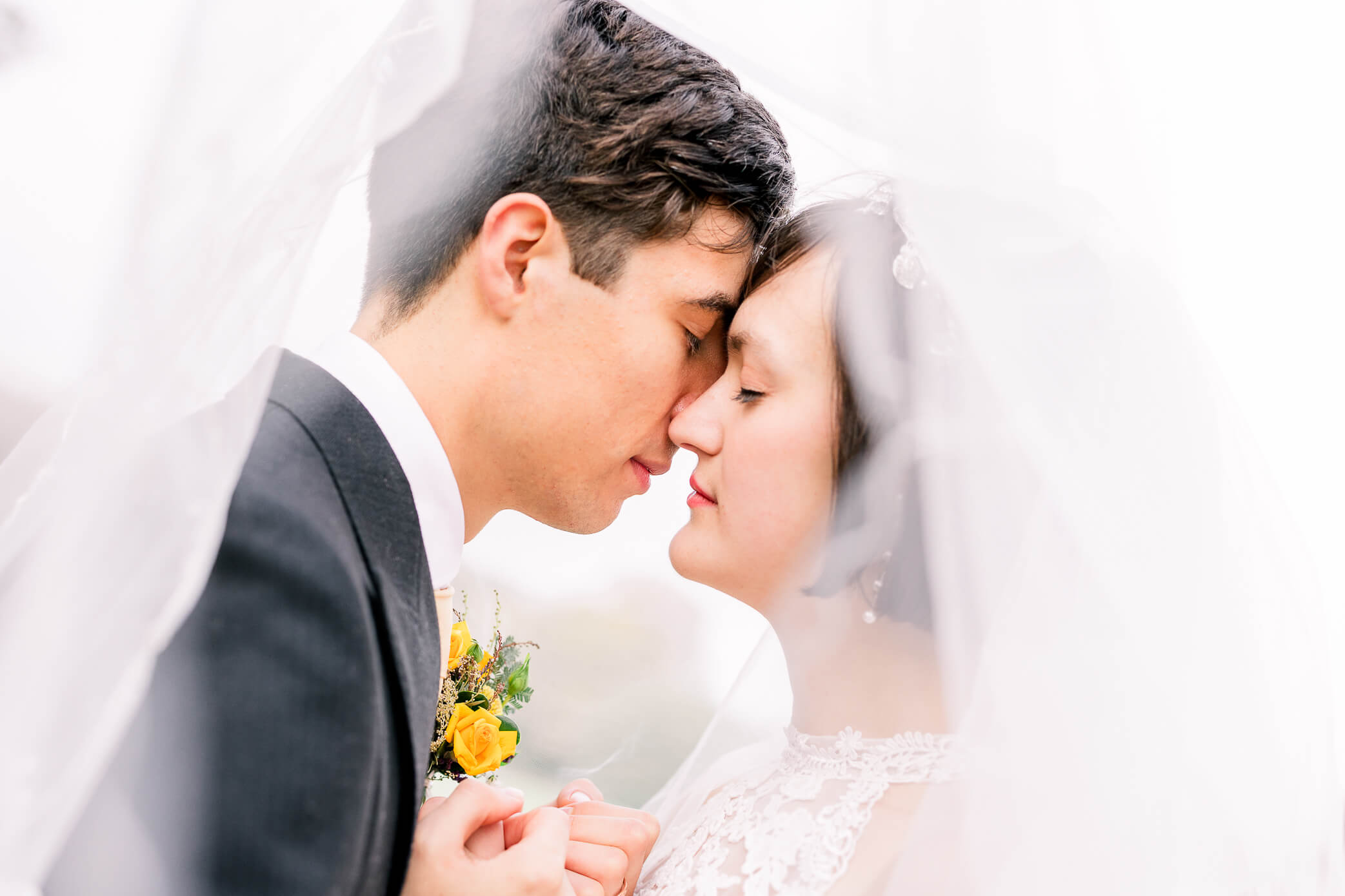 Bride and groom snuggling close for an intimate moment underneath a veil.