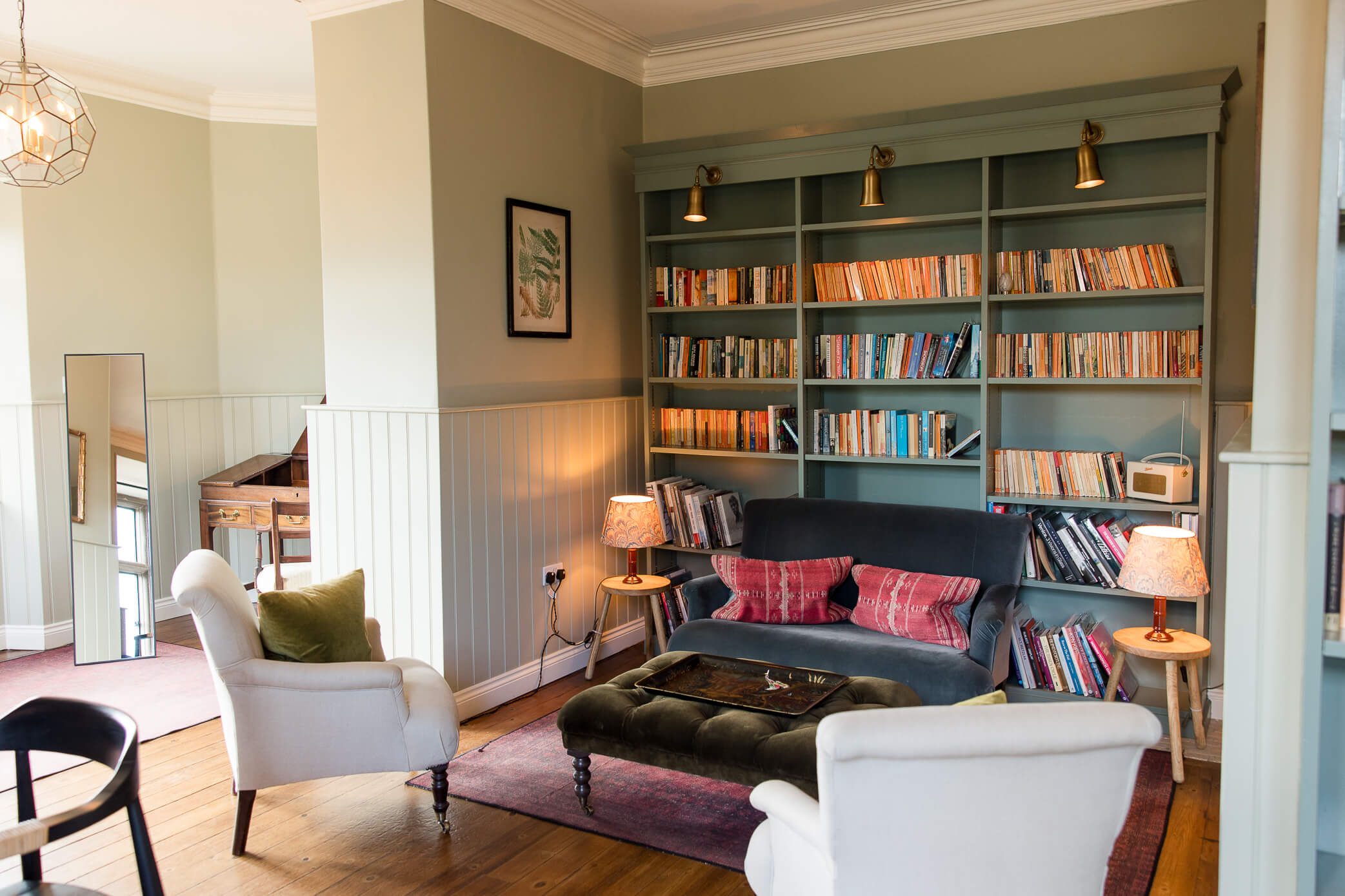 The groom prep room called "the Library" with a green bookshelf wall filled with books and comfortable seating in front of it