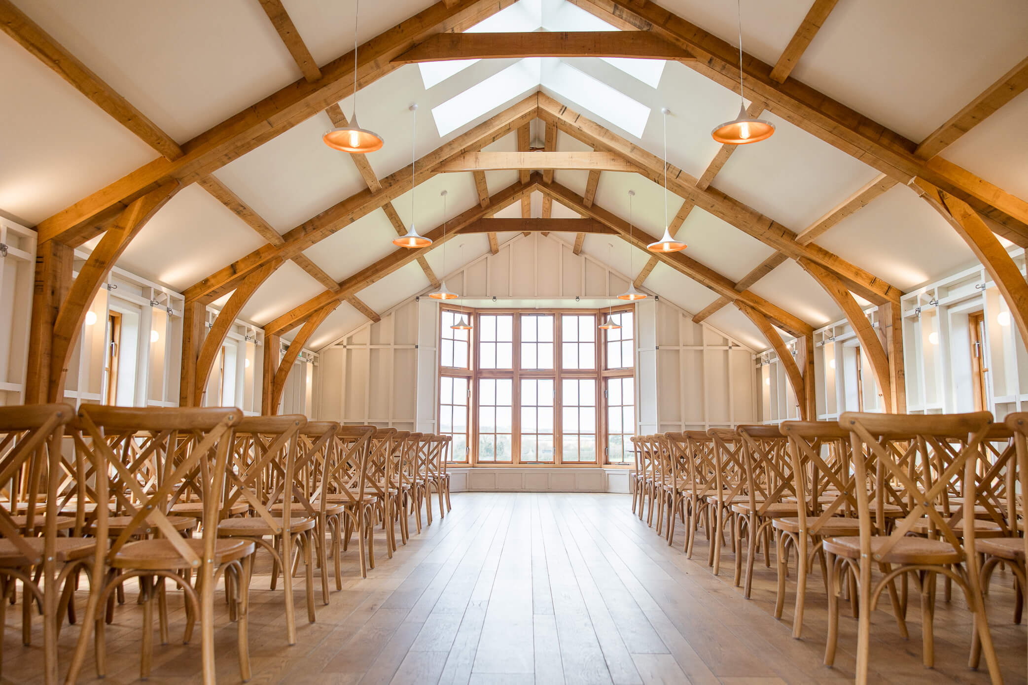 Inside the Grange, which is set up for a wedding ceremony with chairs facing the front. There are warm oak beams above and large bay window at the back.