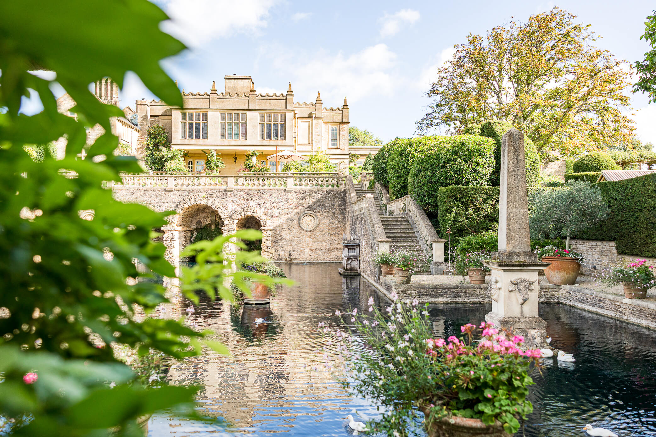 Euridge Manor wedding venue in the Cotswolds, featuring a romantic Italian-inspired garden with a reflective pool, stone staircase, colourful flowers and an elegant manor house.