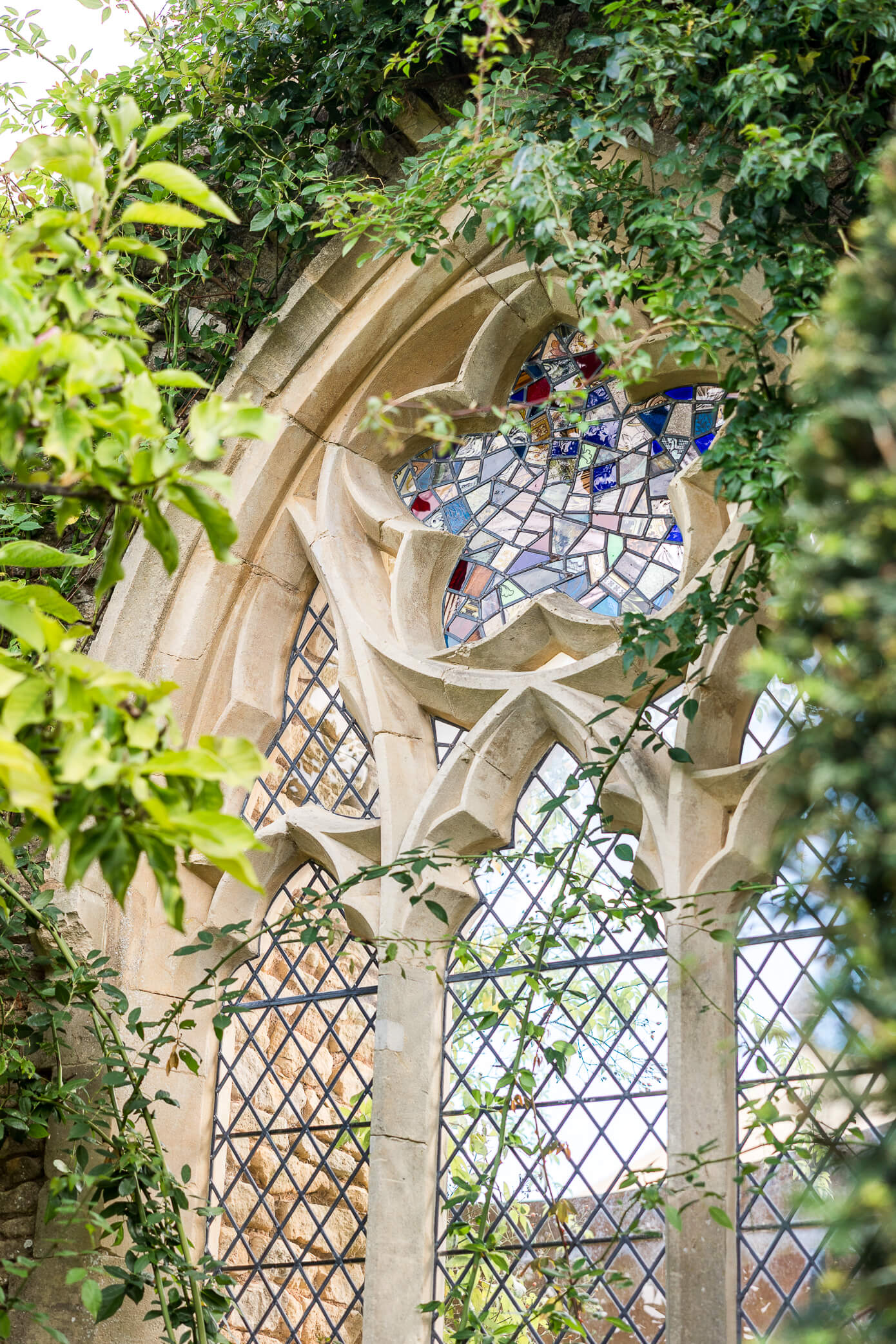 Stained glass star-shaped window inside an arched stone structure, covered in leaves and greenery