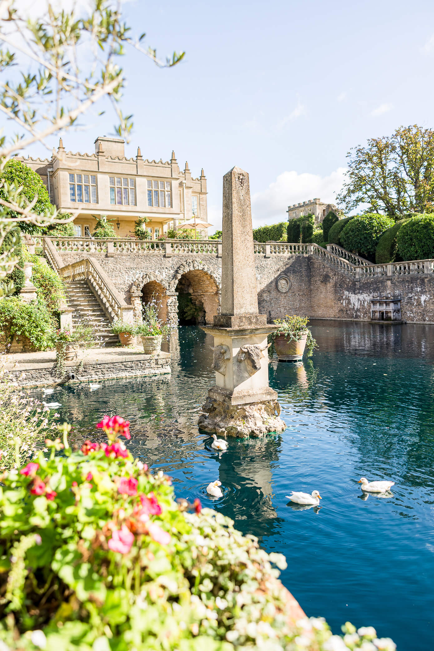 A view of Euridge Manor from the boating house with the teal lake water and white ducks swimming.